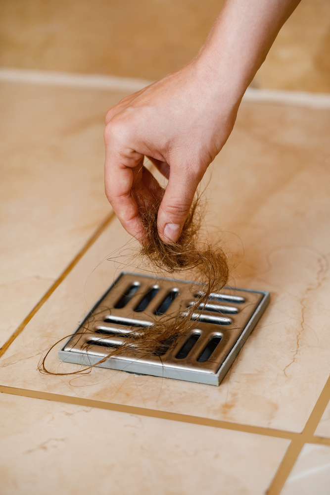 woman pulling hair out of shower drain