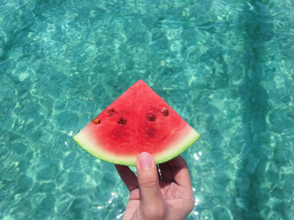 person holding watermelon slice over pool